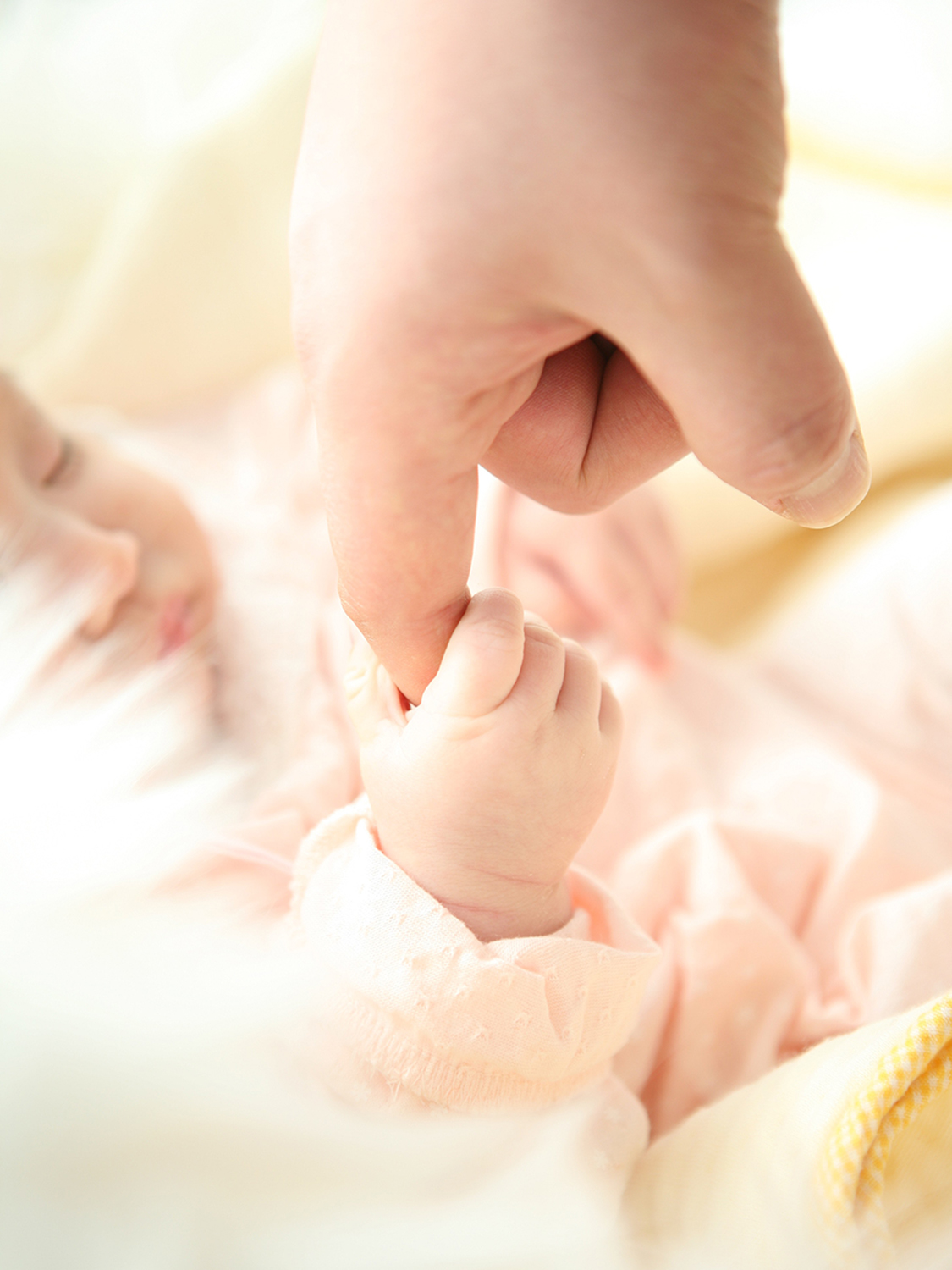 Baby holding parents finger in a pink onsie